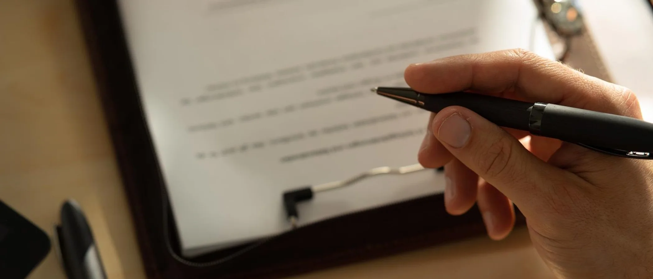 A hand signing a document on a leather padfolio with a fine pen in warm light