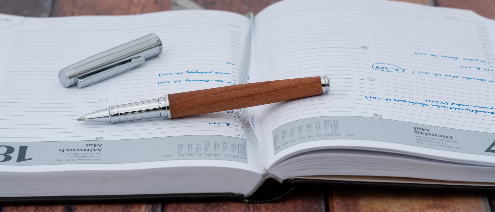 A real-wood pen resting on an open, handwritten planner on a warm wooden desk