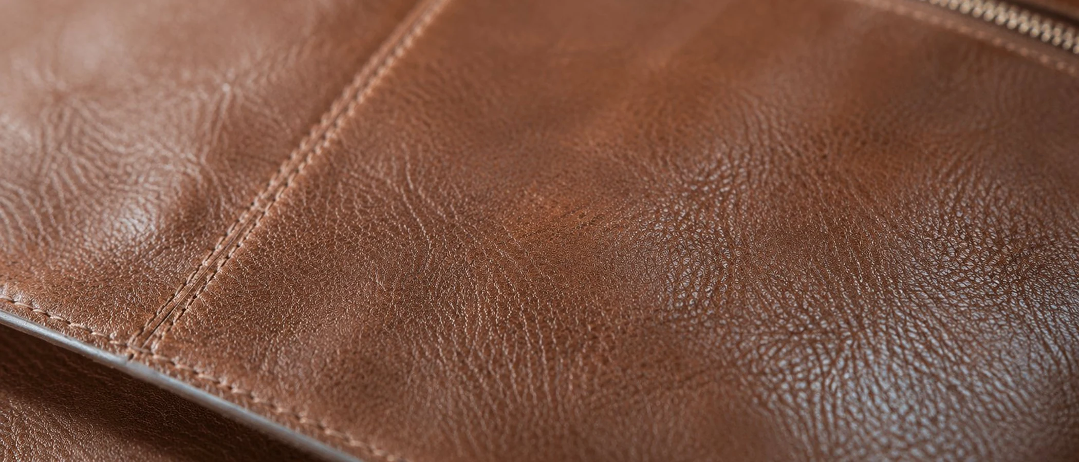 Close-up of warm cognac leather grain with a seam, softened by use