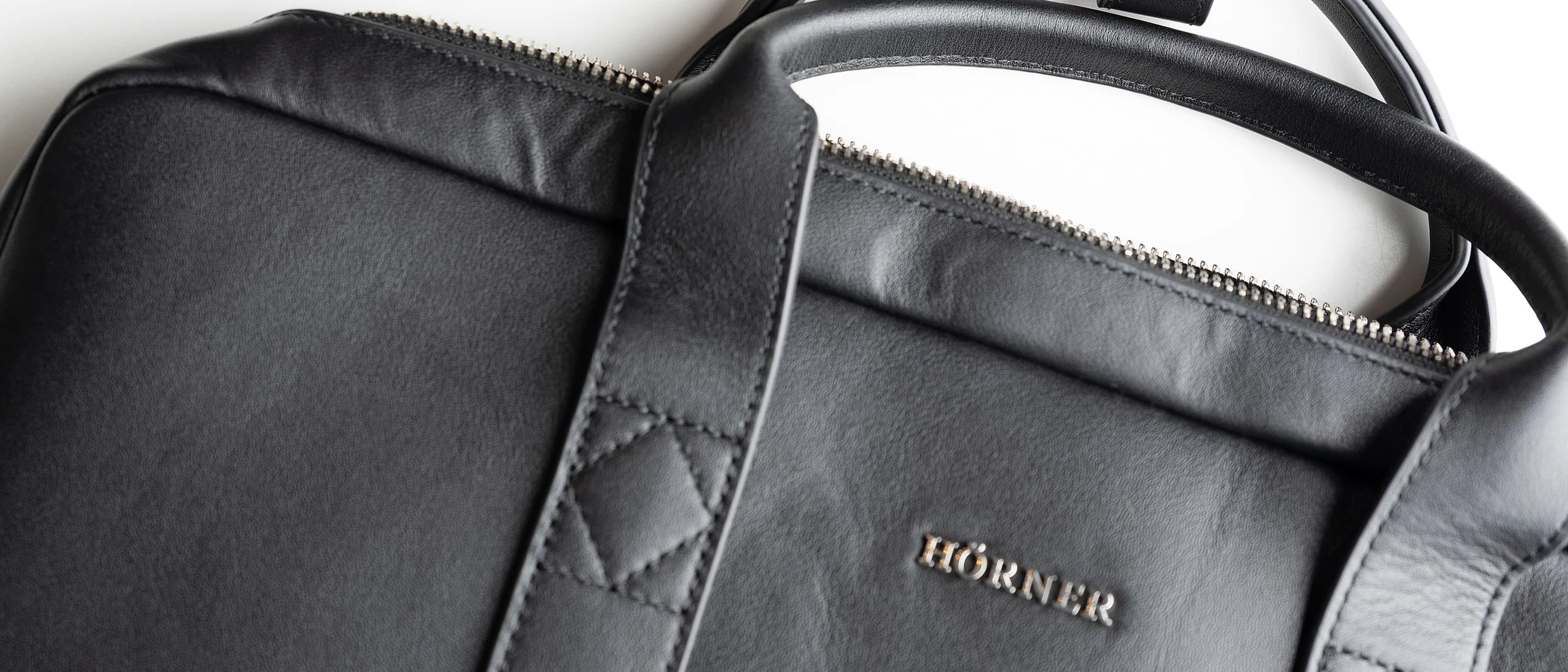 Close-up of a black leather Hörner Mainz business bag, showing the handles, zip and embossed logo