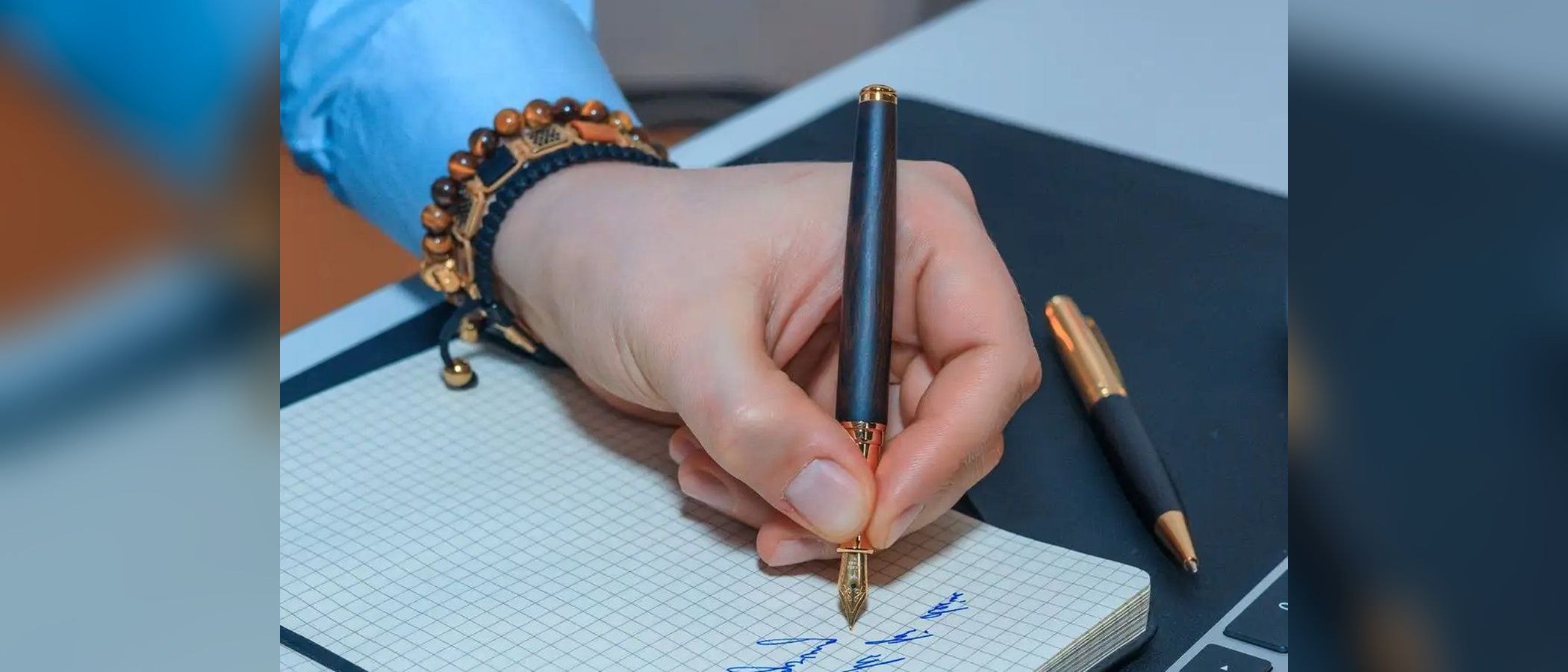 A left hand writing with an ebony fountain pen in a squared notebook