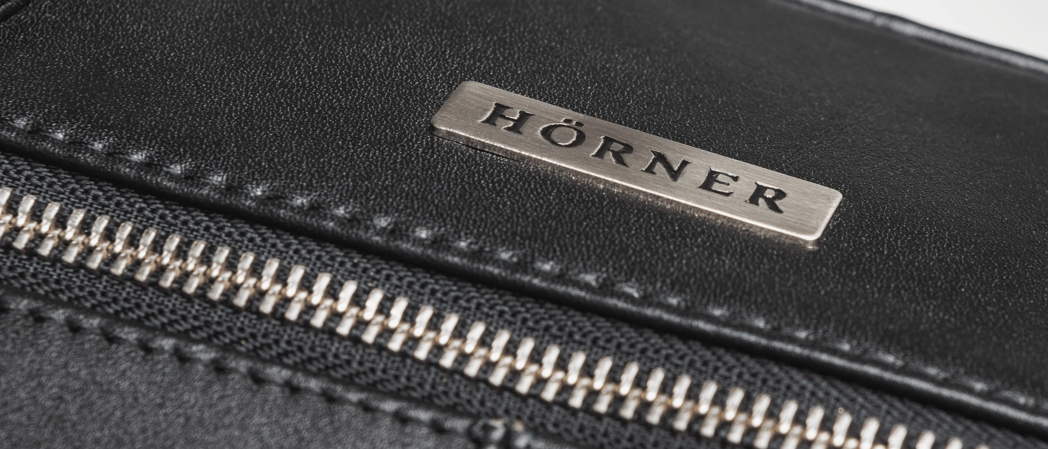 Close-up of smooth black nappa leather with the embossed Hörner mark and a zip