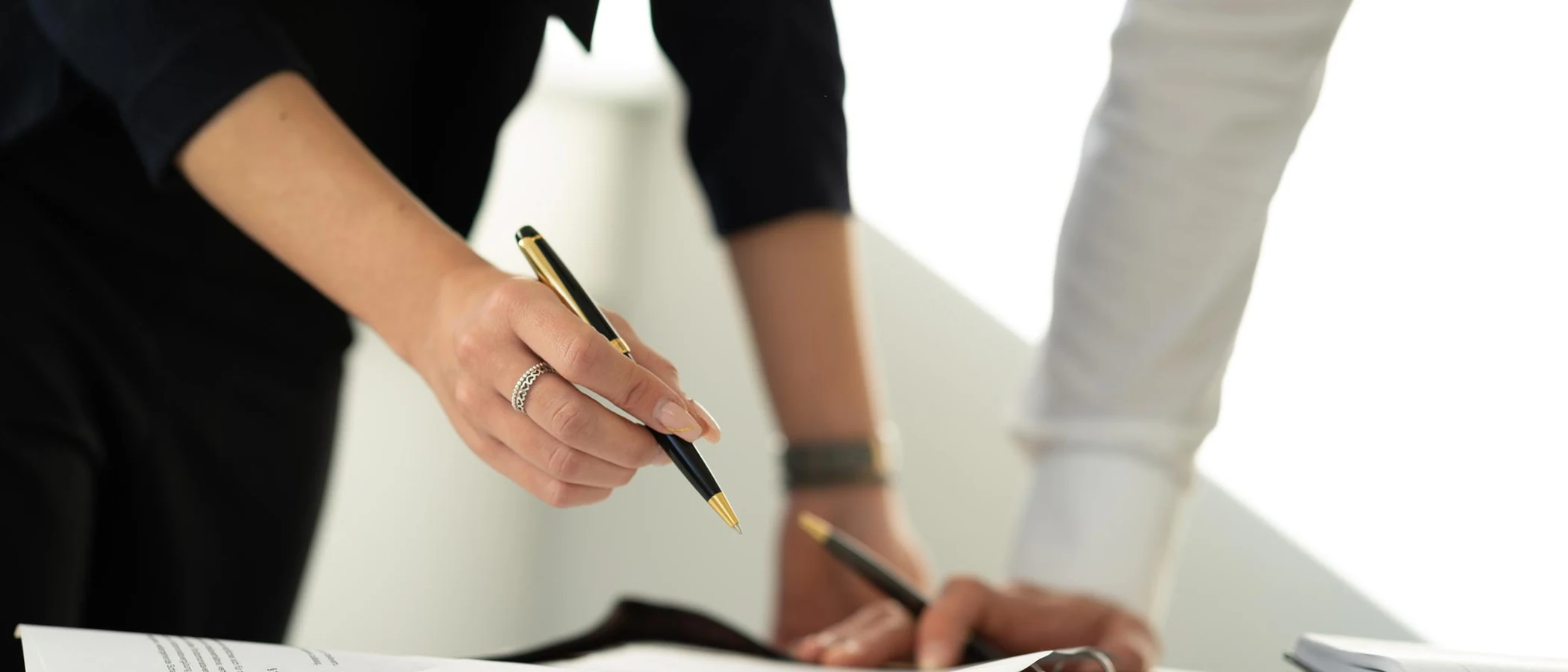 A hand signing a document with a black and gold Hörner pen