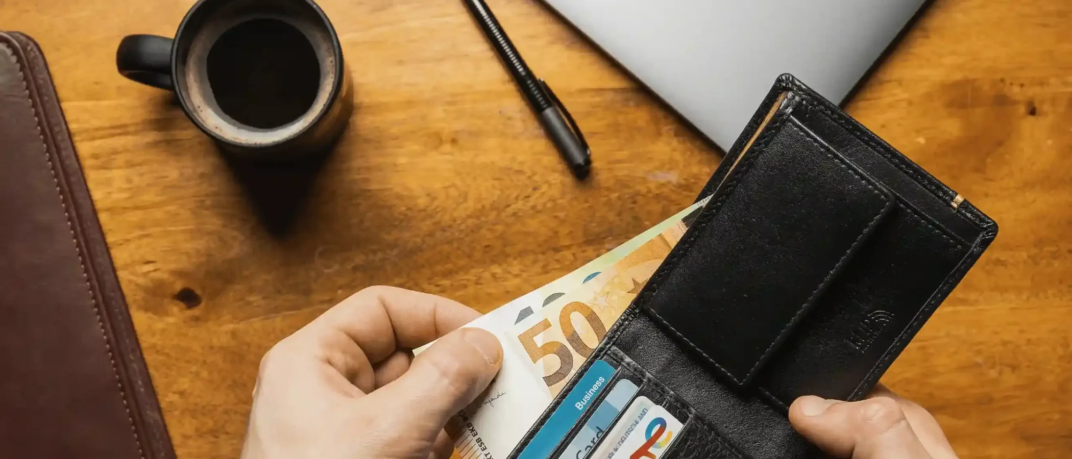Hands holding an open black leather wallet full of contactless bank cards and a note on a desk