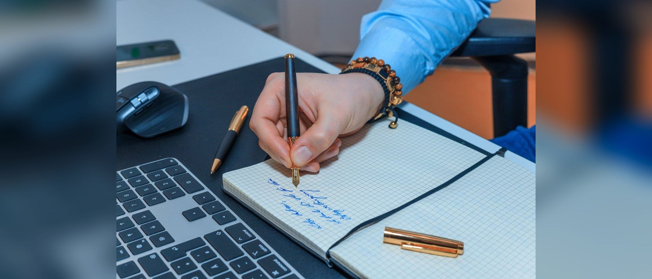 A hand signing a notebook with a wooden fountain pen at a desk