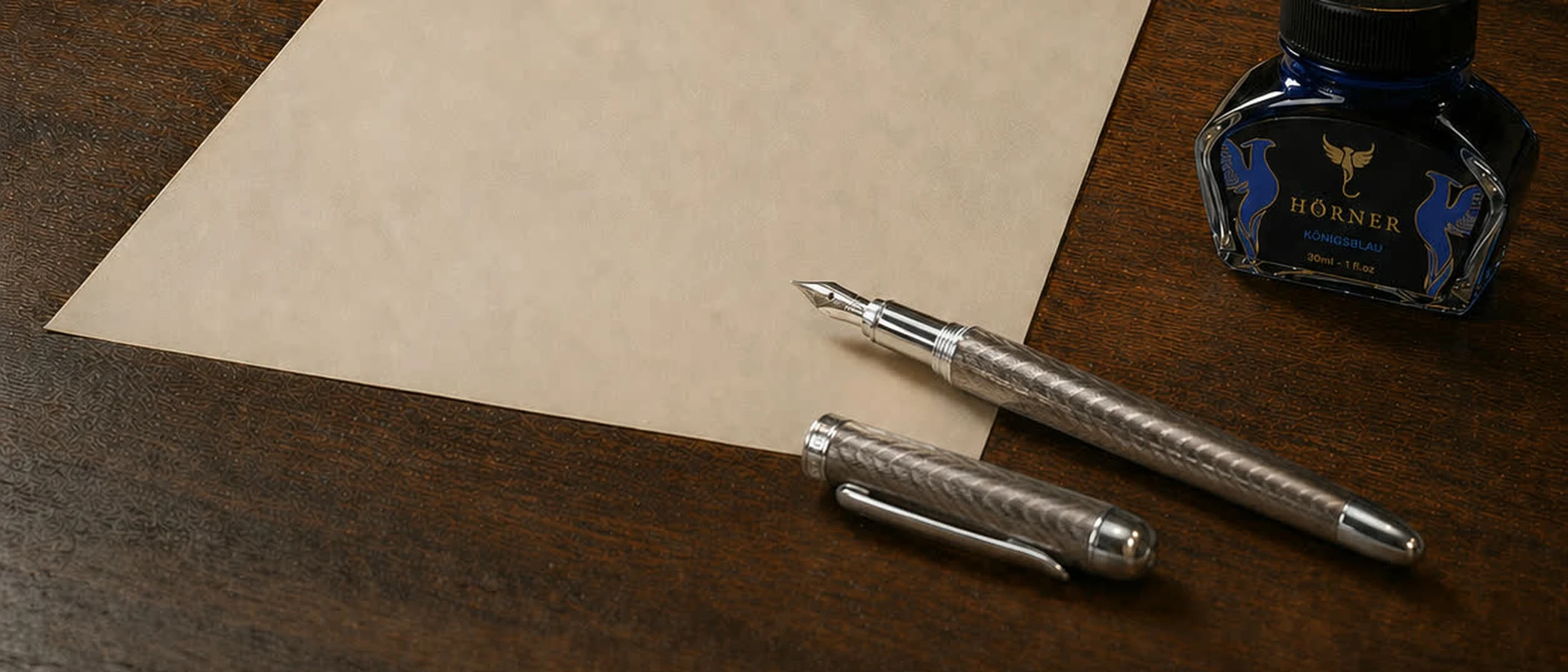 A blank sheet of cream paper on a dark desk with a fountain pen and a bottle of ink