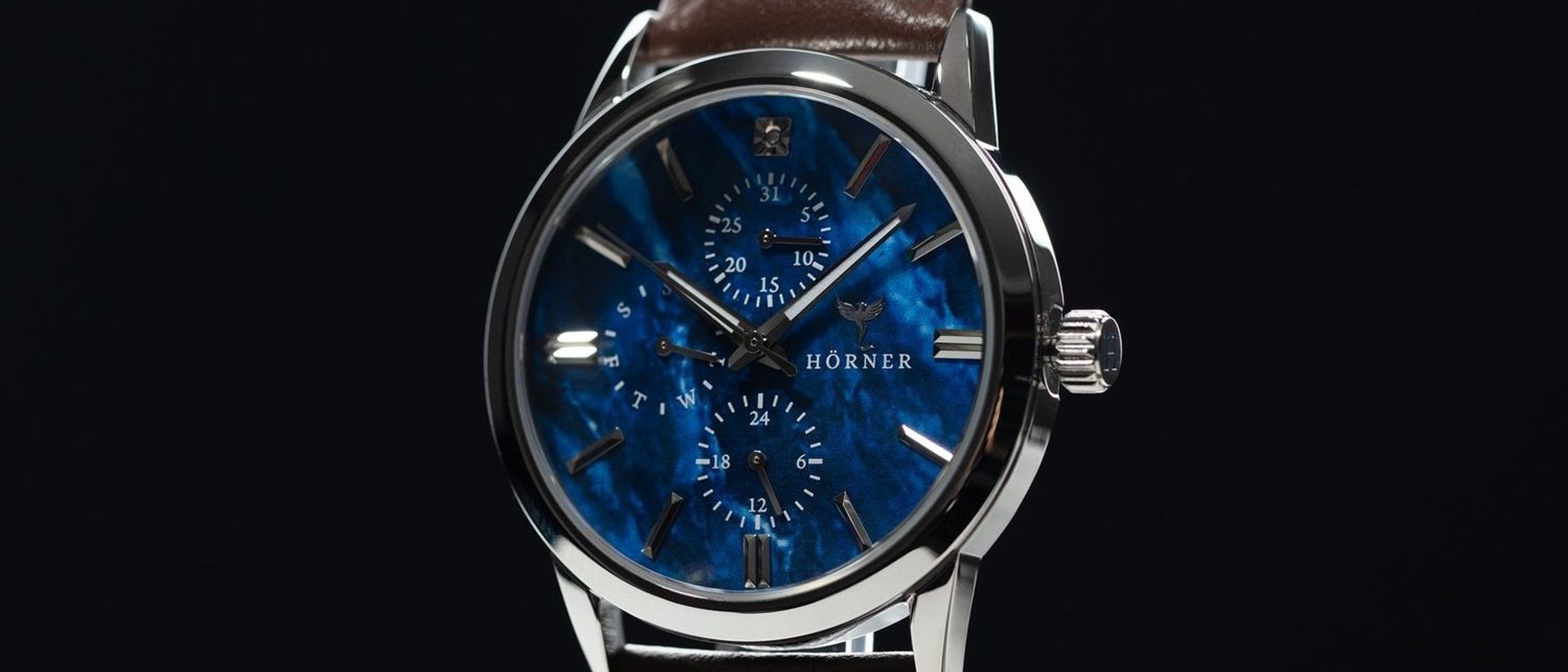A close view of a watch with a deep blue dial under a clear sapphire crystal