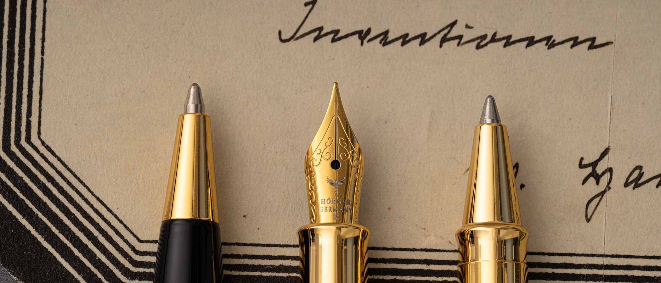 The tips of a Hörner ballpoint, gold fountain-pen nib and rollerball side by side on antique handwriting